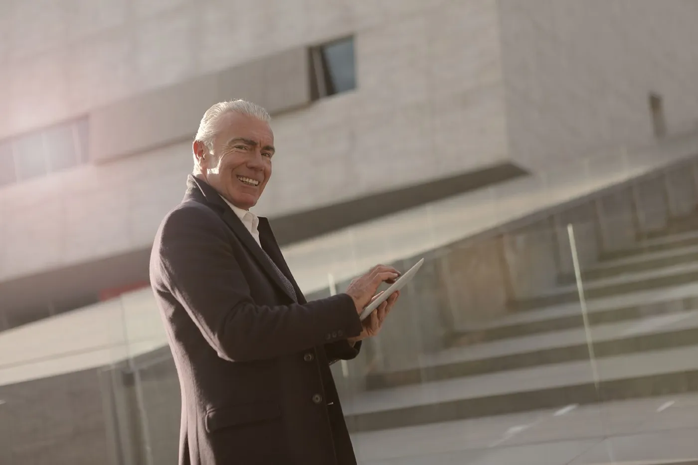 Executivo sorrindo enquanto usa um tablet em frente a um edifício corporativo